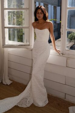 bride in strapless lace wedding gown standing by window